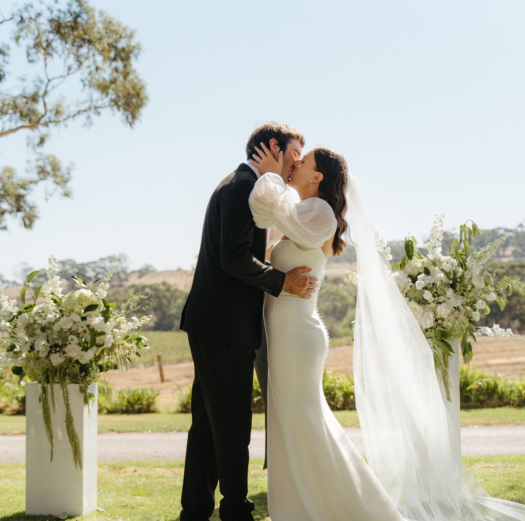 Couple kissing outdoors with floral arrangements on a sunny day